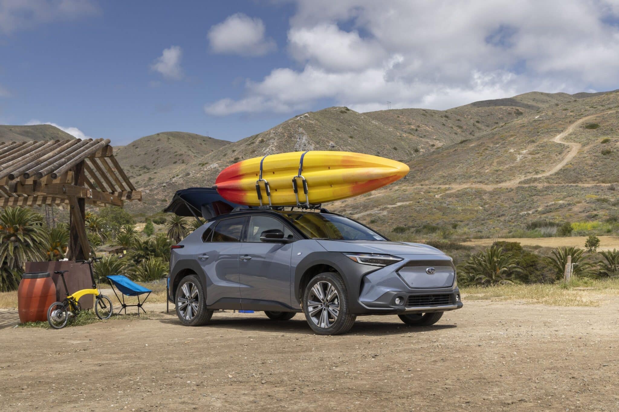 A Subaru Solterra with a kayak on its roof and camping supplies nearby.